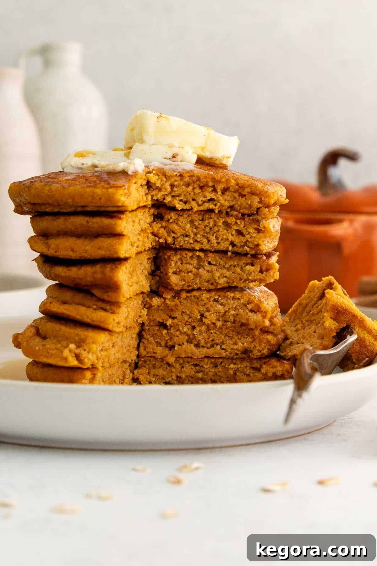 Spiced Oat Flour Pumpkin Pancakes 8 A close-up of a stack of fluffy oat flour pumpkin pancakes with a small section cut out, and a fork lifting a bite, showcasing the tender, moist interior.