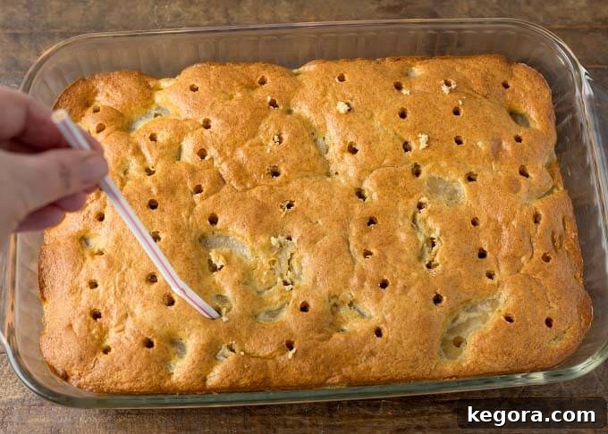Spiced Caramel Apple Poke Cake 5 A hand using a drinking straw to poke evenly spaced holes into a freshly baked, unfrosted cake in a glass baking dish, preparing it for caramel infusion.