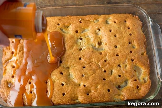Spiced Caramel Apple Poke Cake 6 A generous amount of caramel sauce being poured and spread evenly over the poked holes of a baked cake in a glass dish, ensuring deep penetration.