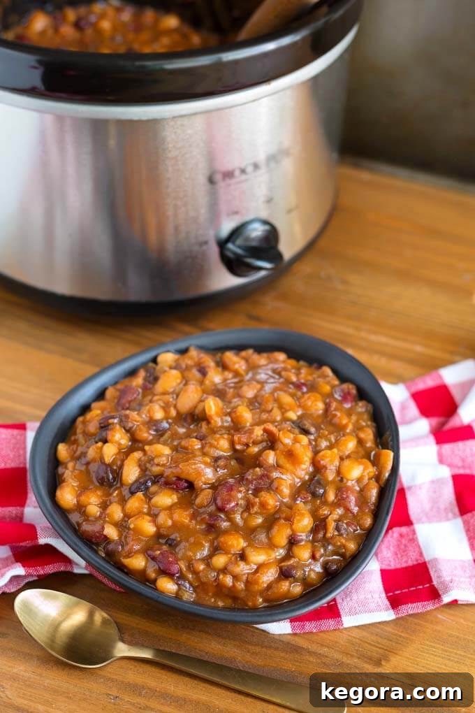 Hearty serving of slow cooker baked beans in a black bowl on a red gingham napkin for a picnic