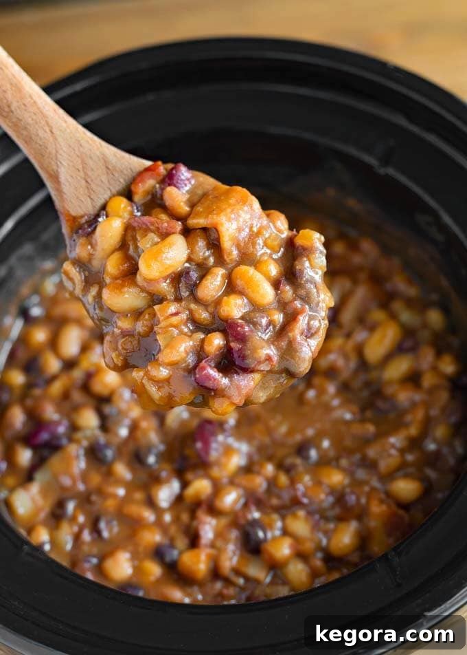 Close-up of savory baked beans being stirred with a wooden spoon in a slow cooker