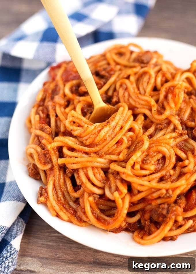 Instant Pot Spaghetti in white bowl with golden fork next to blue gingham napkin