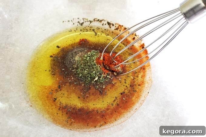 Mixing olive oil, salt, pepper, garlic powder, onion powder, paprika, and dried basil leaves in a glass bowl.