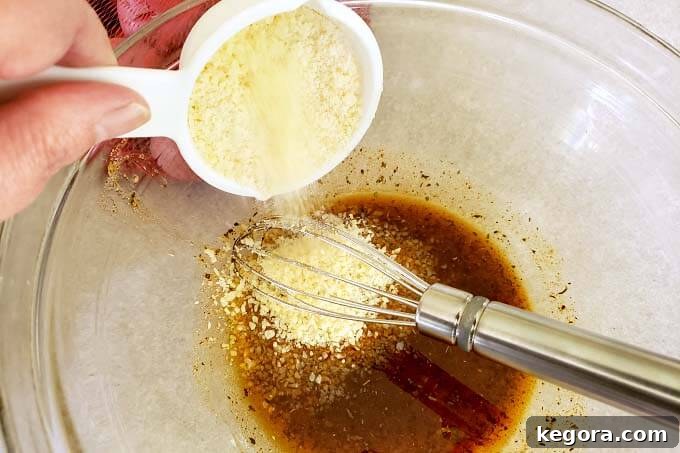 Adding grated Parmesan cheese to the spice and oil mixture in a glass bowl.