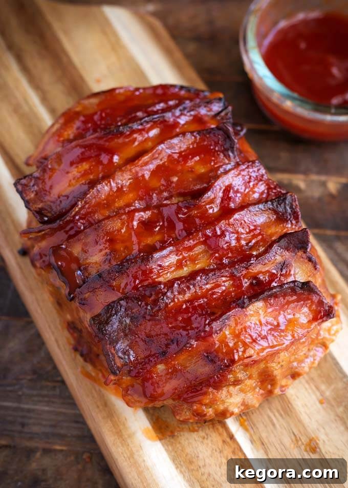 Turkey Meatloaf topped with crispy bacon strips on a rustic wooden board, ready to be sliced