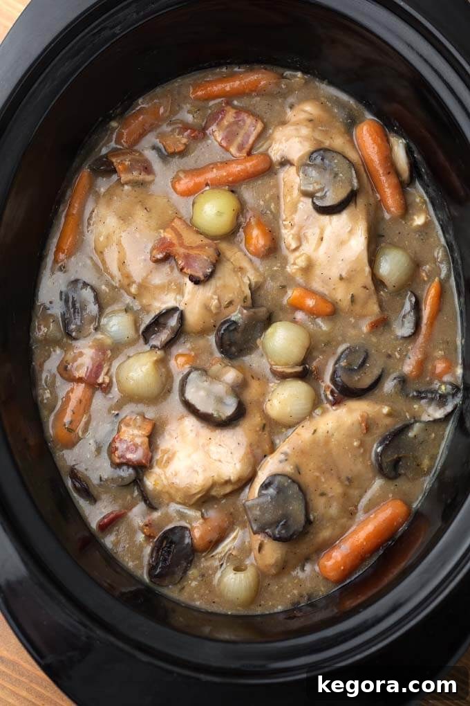 Effortless Slow Cooker Coq Au Vin 4 Close-up of Slow Cooker Coq Au Vin in a black slow cooker, showing the rich sauce, chicken, mushrooms, and pearl onions.