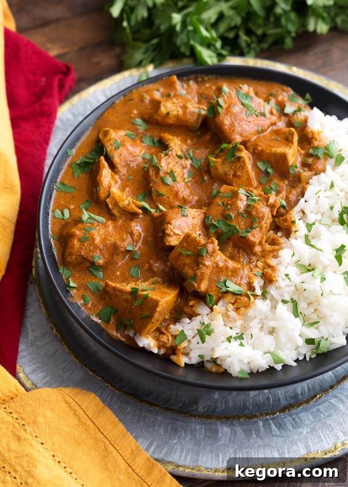 Indian Butter Chicken with rice on a black plate, garnished with fresh cilantro.