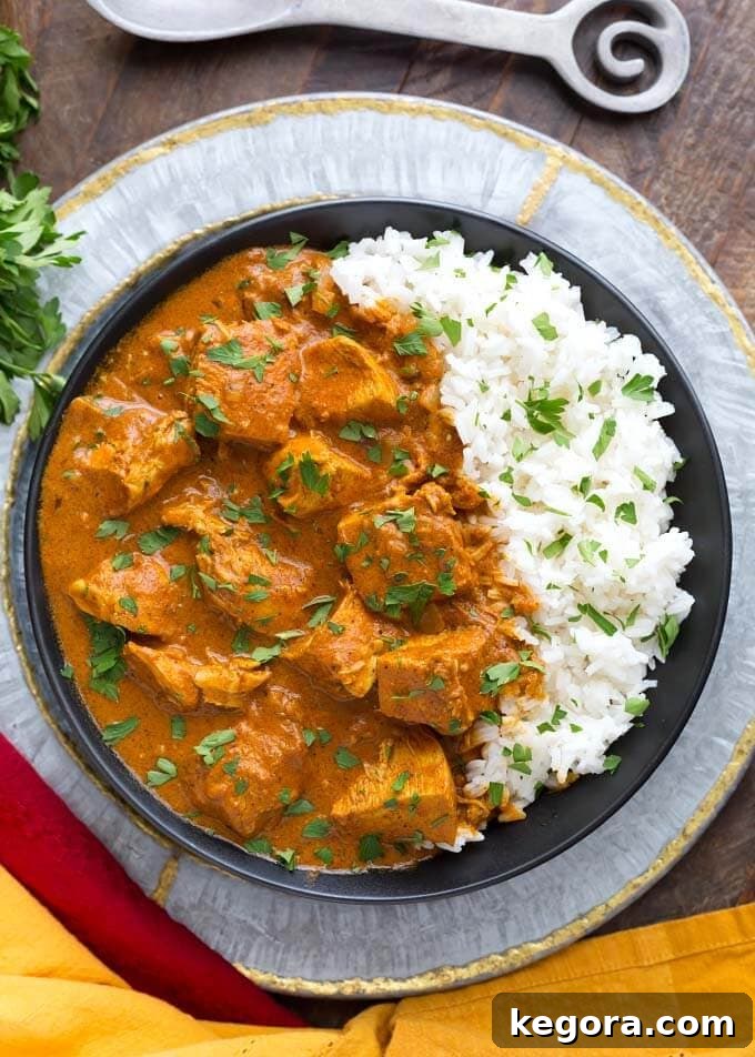 Indian Butter Chicken served with white rice on a black plate, placed on a decorative silver platter, ready to eat.