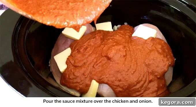 Pouring the prepared creamy, spiced sauce over chicken and onions in a slow cooker, ready for cooking.
