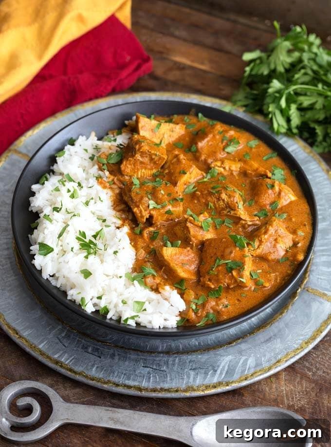 Slow Cooker Indian Butter Chicken with rice on a black plate, artfully arranged on a silver platter, garnished with fresh herbs.