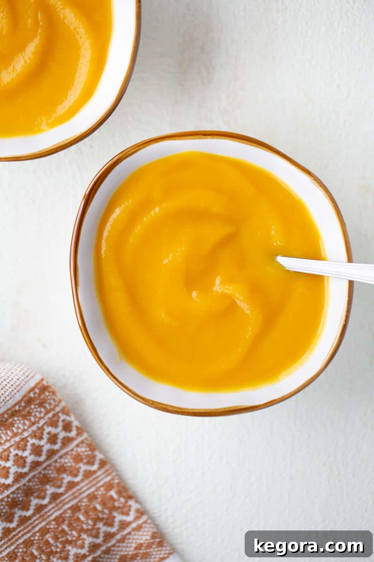 close up shot of butternut squash leek soup in a white bowl, garnished with fresh herbs