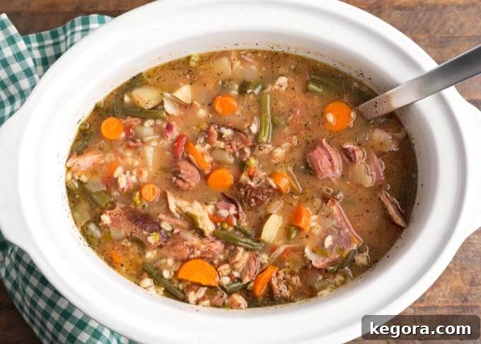 Ham Vegetable Barley Soup served directly from a white slow cooker with a ladle
