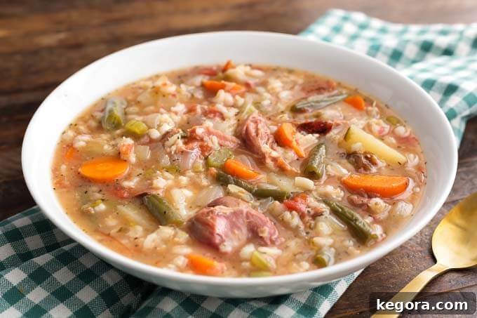 Slow Cooker Ham Vegetable Barley Soup in a white bowl with a spoon on a green gingham napkin, close-up