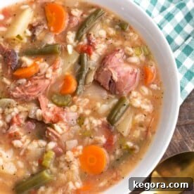 Slow Cooker Ham Vegetable Barley Soup in white bowl on top of green gingham napkin