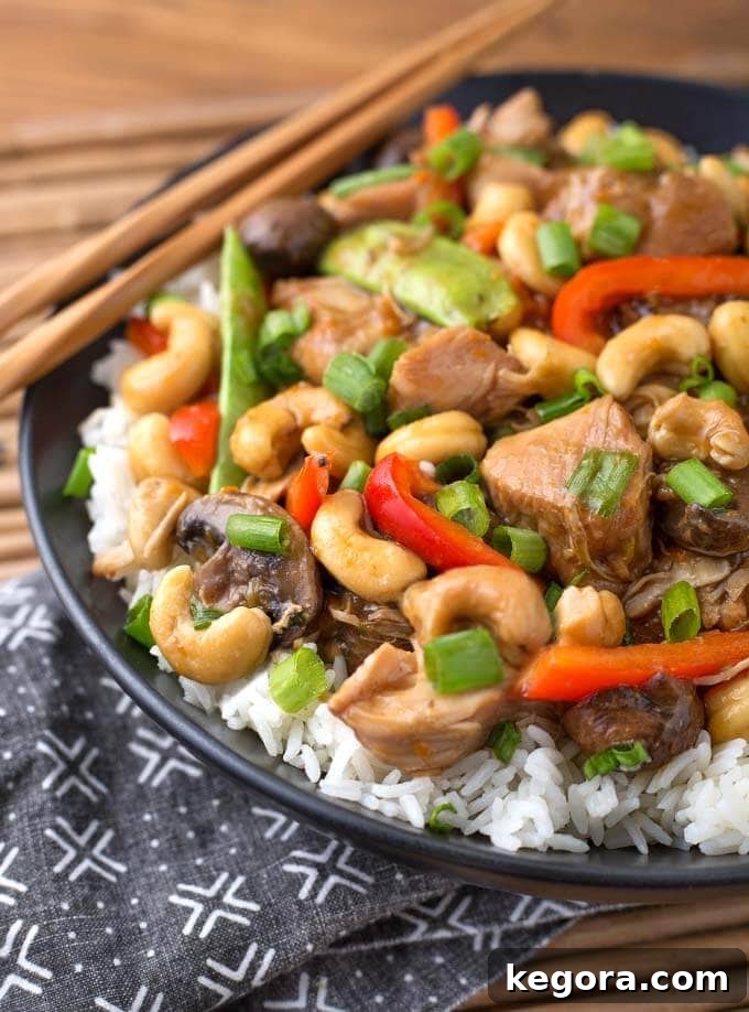 Quick and Delicious Instant Pot Cashew Chicken 4 Close up of Instant Pot Cashew Chicken over rice on black plate with wooden chopsticks, showing cashews and green onions
