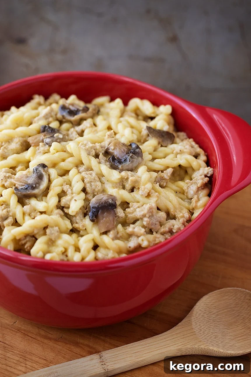 A vibrant red bowl filled with creamy Instant Pot Cheeseburger Pasta, garnished with fresh herbs, resting on a rustic wooden board with a wooden serving spoon beside it.