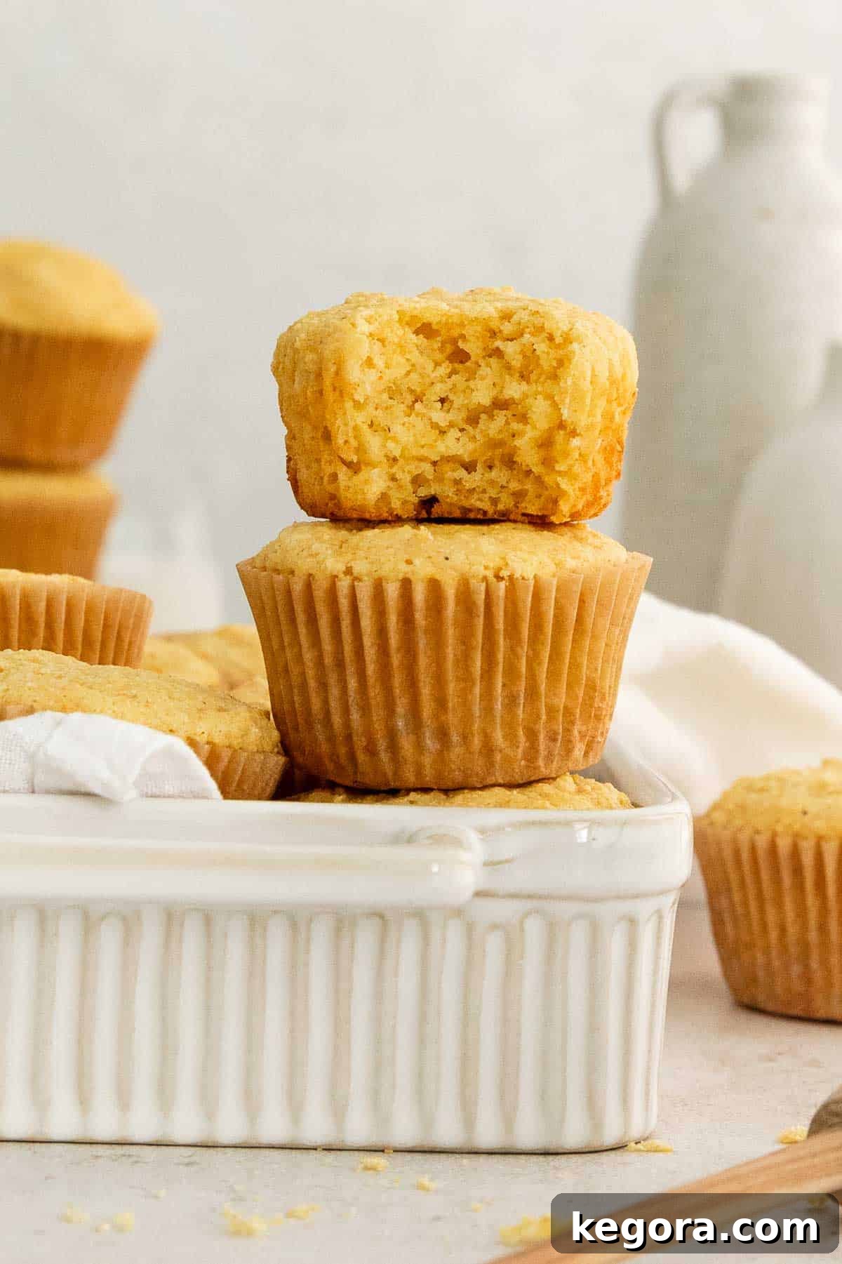Two golden corn muffins stacked on a dish of more muffins, one with a bite taken out.
