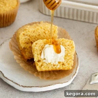A gluten-free corn muffin sliced in half, revealing its tender interior, served with butter and honey.