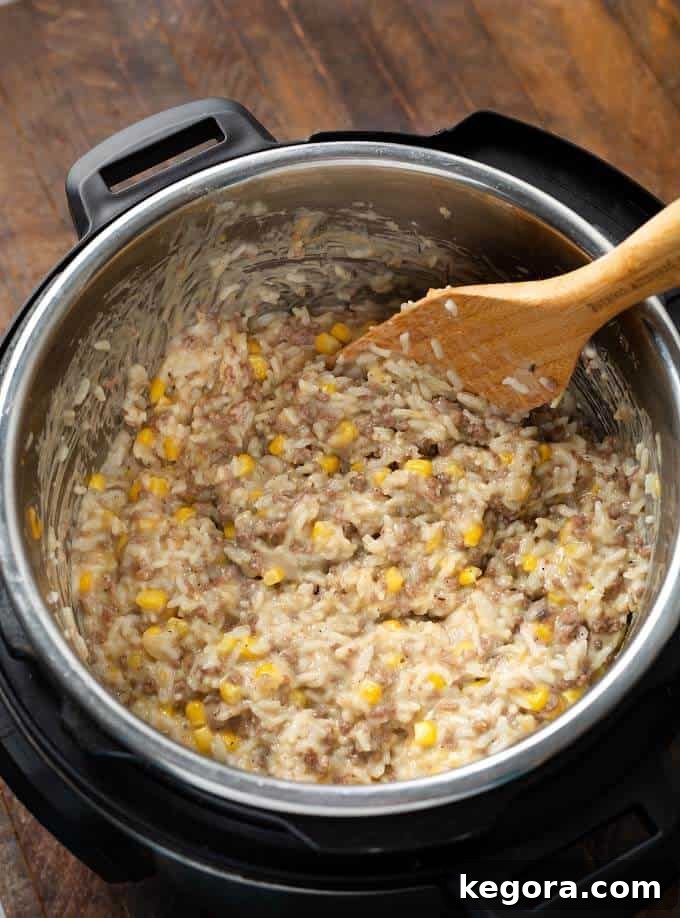 Instant Pot Cheesy Hamburger Rice Casserole being stirred in the pressure cooker pot with a wooden spoon.