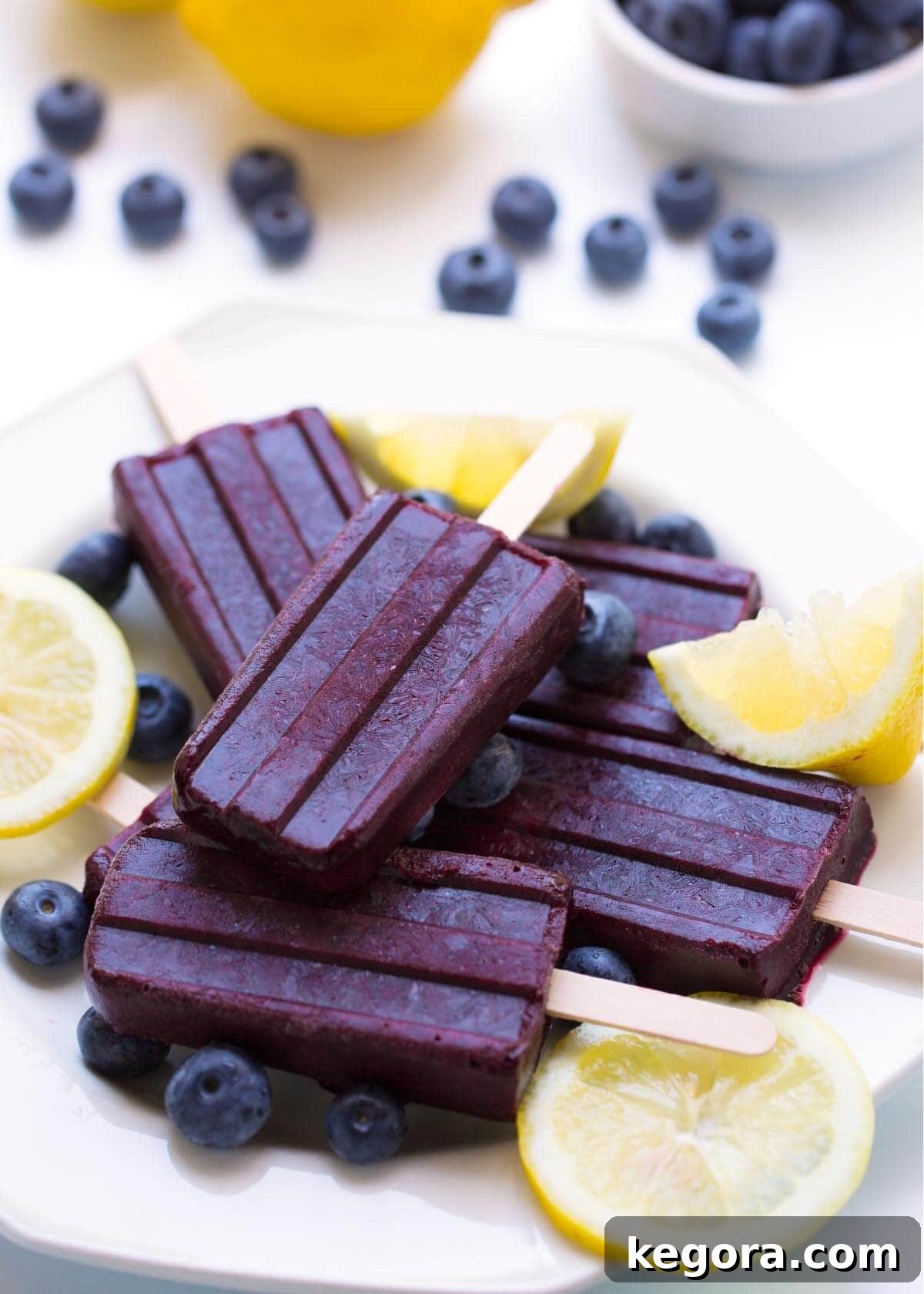 Sun-Kissed Berry Lemon Freezes 2 Five Blueberry Lemon Popsicles on a white plate with lemon slices and blueberries