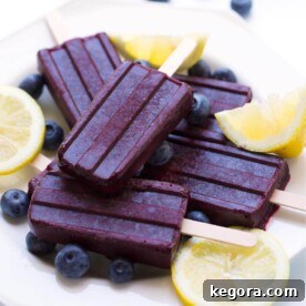 Five Blueberry Lemon Popsicles on a white plate with lemon slices and blueberries