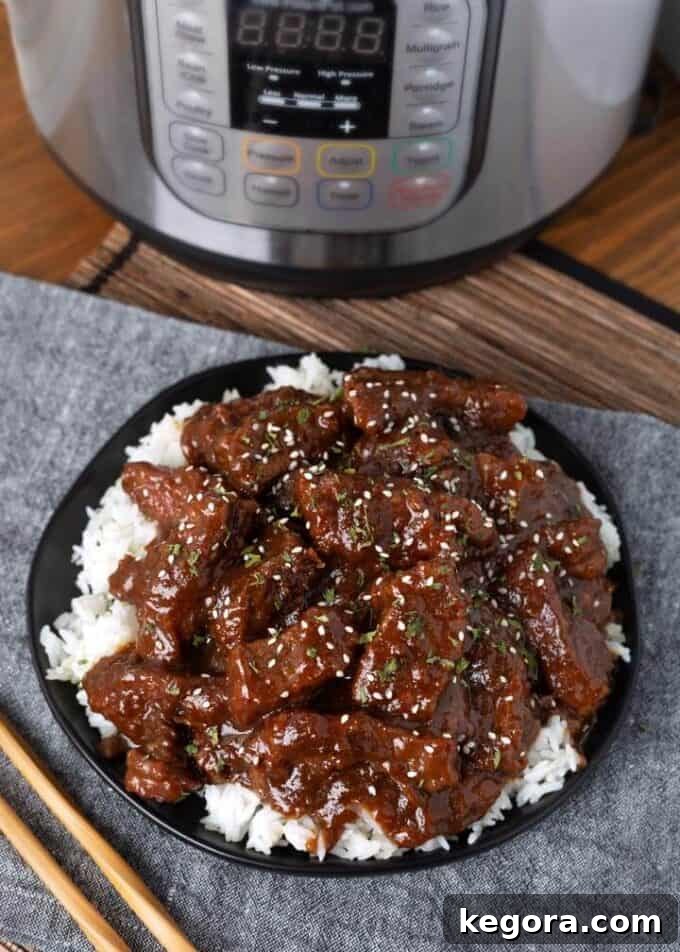 Restaurant-Style Instant Pot Mongolian Beef 2 Pressure Cooker Mongolian Beef over rice on black plate next to wooden chopsticks