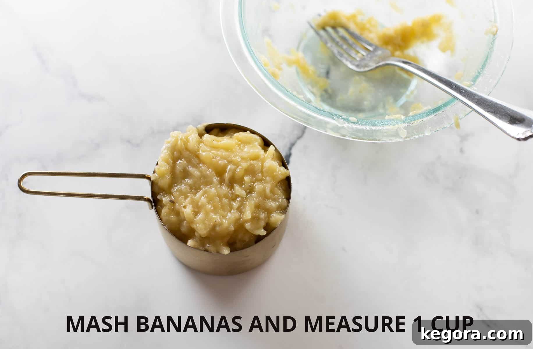 Mashed banana in a gold measuring cup on a marble background