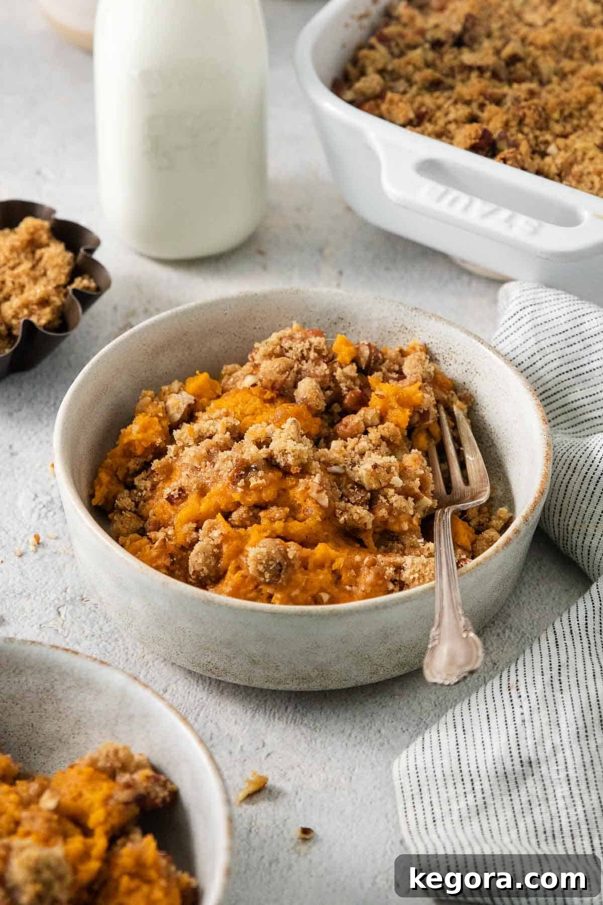 The Ultimate Gluten-Free Sweet Potato Casserole with Praline Pecan Crunch 3 A serving of gluten-free sweet potato casserole in a bowl with a fork, ready to be enjoyed.