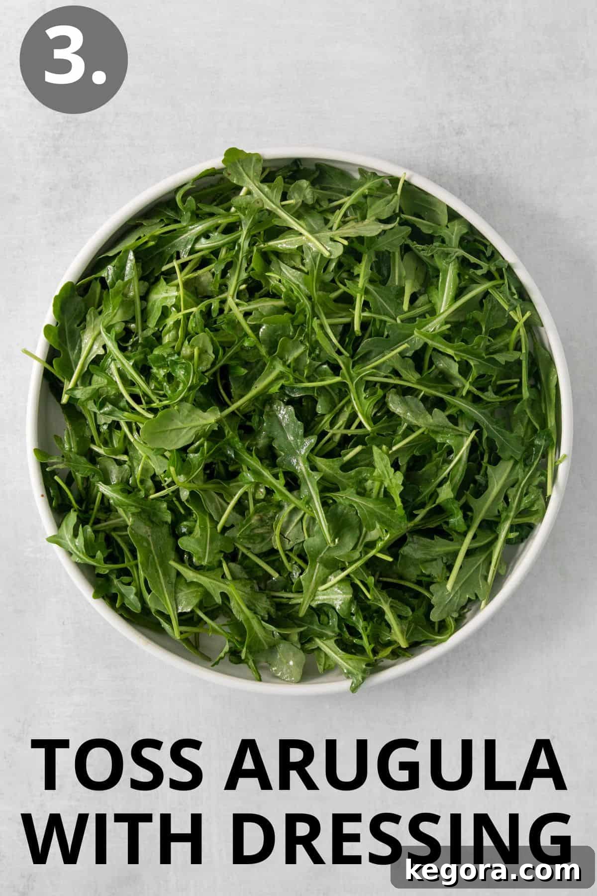 Arugula and a portion of dressing mixed together in a large white bowl