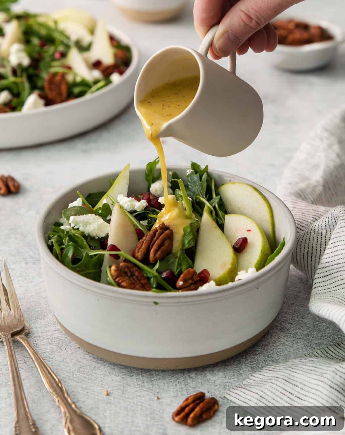 A hand pouring dressing over arugula pear salad in a bowl