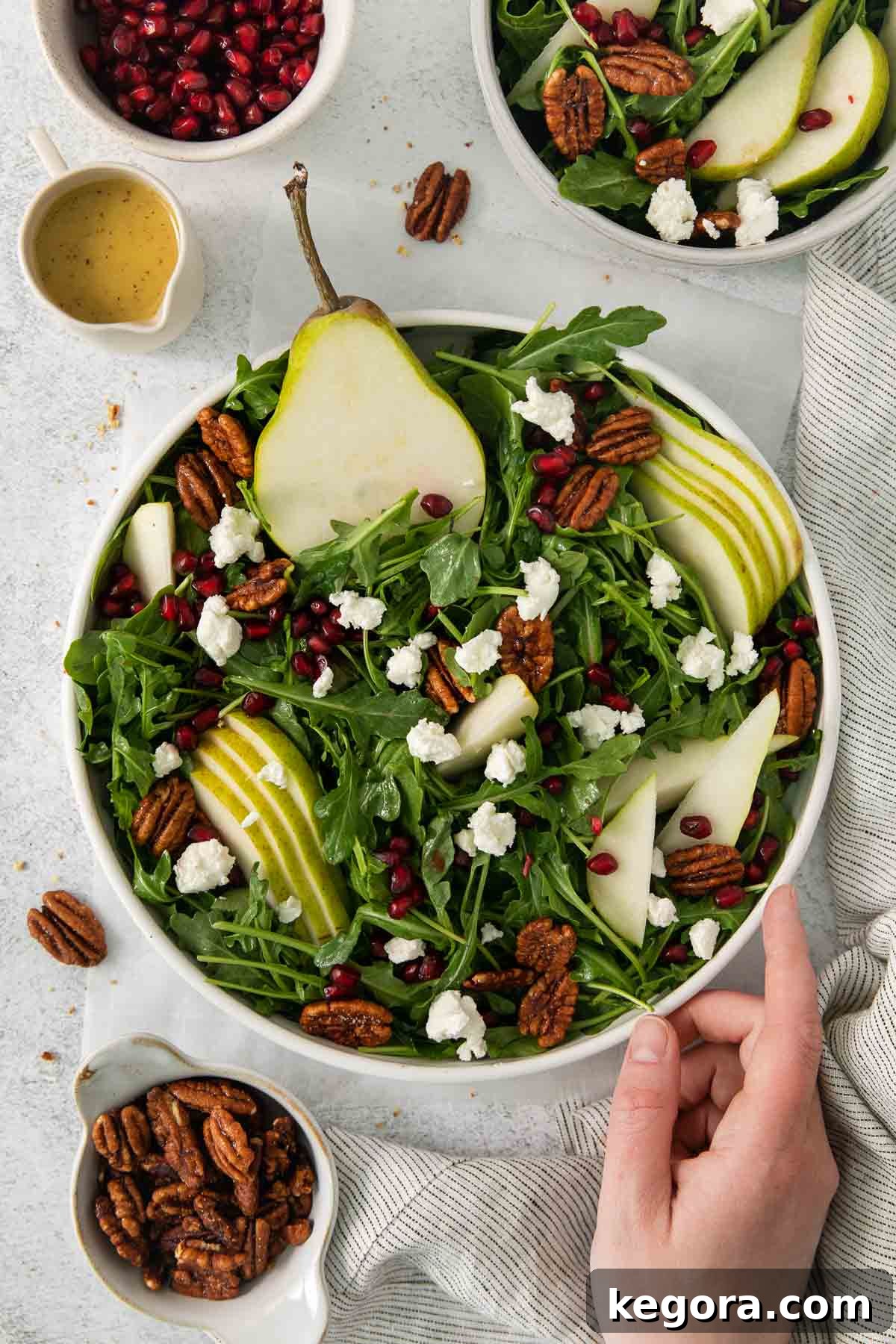 A hand gently touching the freshly made arugula pear salad in a bowl