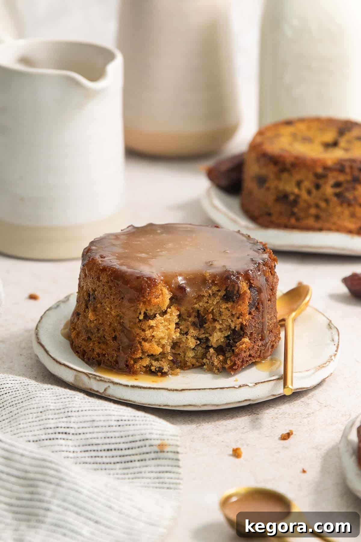 Gluten-free sticky toffee pudding on a plate with a spoon next to it, drizzled with toffee sauce and cream