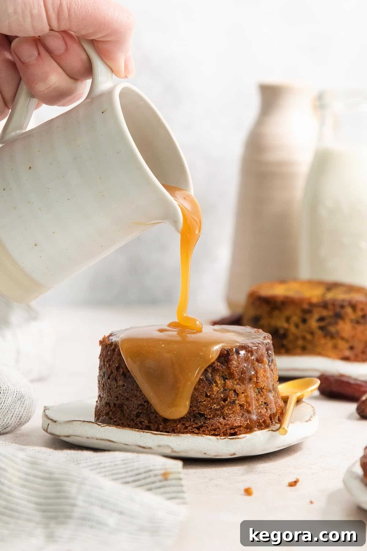 Gluten-free sticky toffee pudding on a plate with a hand pouring sauce over the top