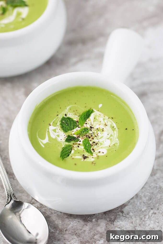 Minty Pea Soup in small white bowl with handle with a silver spoon on a grey stone background