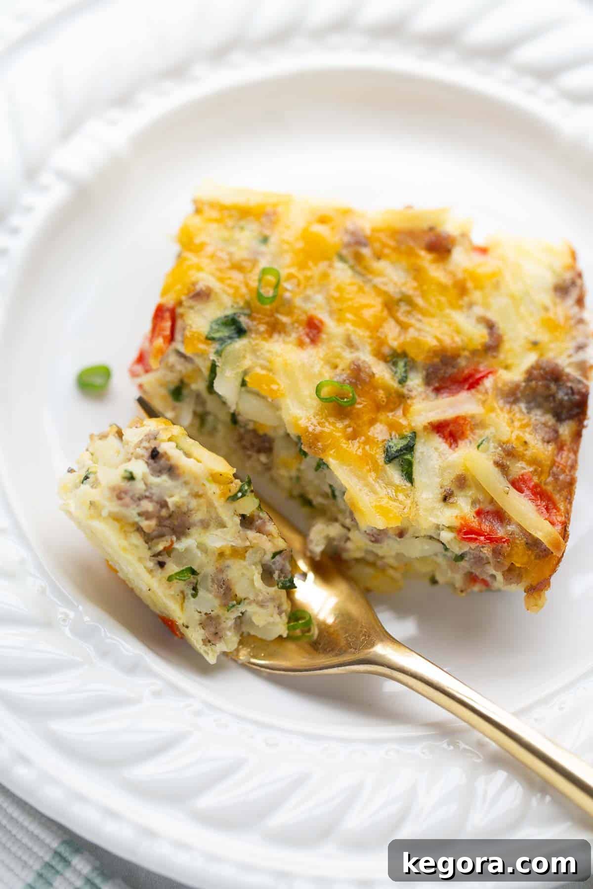 breakfast casserole on white plate with gold fork.