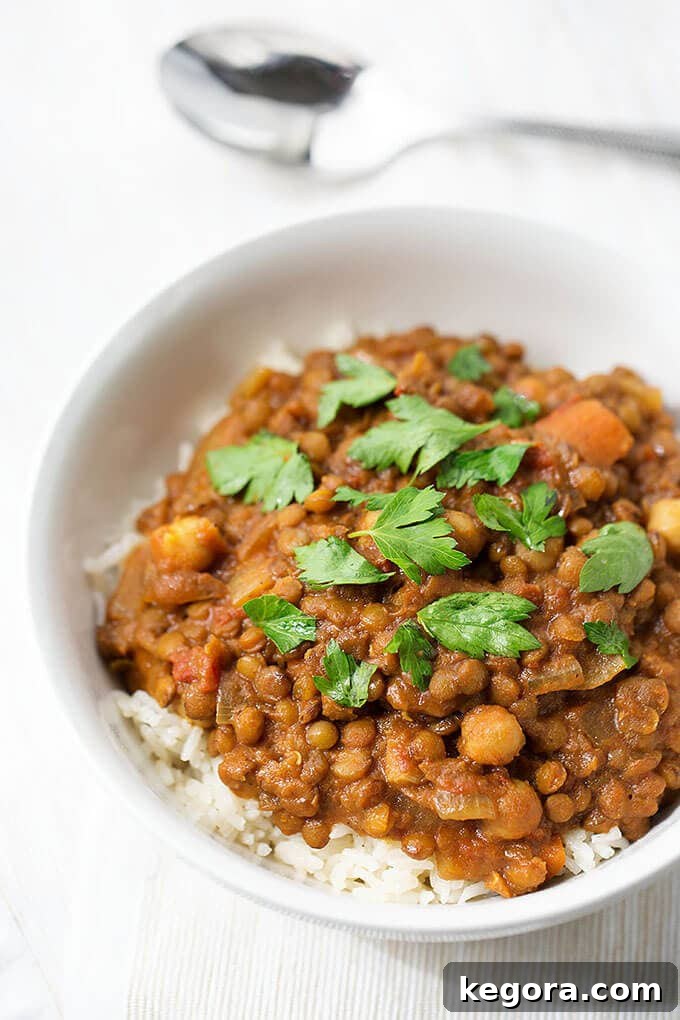 A small white bowl filled with Crock Pot Curry Lentils served over fluffy white rice, garnished with fresh herbs