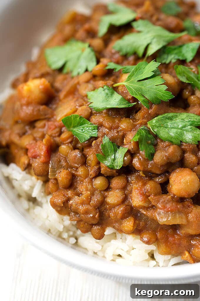 Close-up view of Crock Pot Curry Lentils served over rice in a white bowl, showcasing the rich texture and vibrant colors