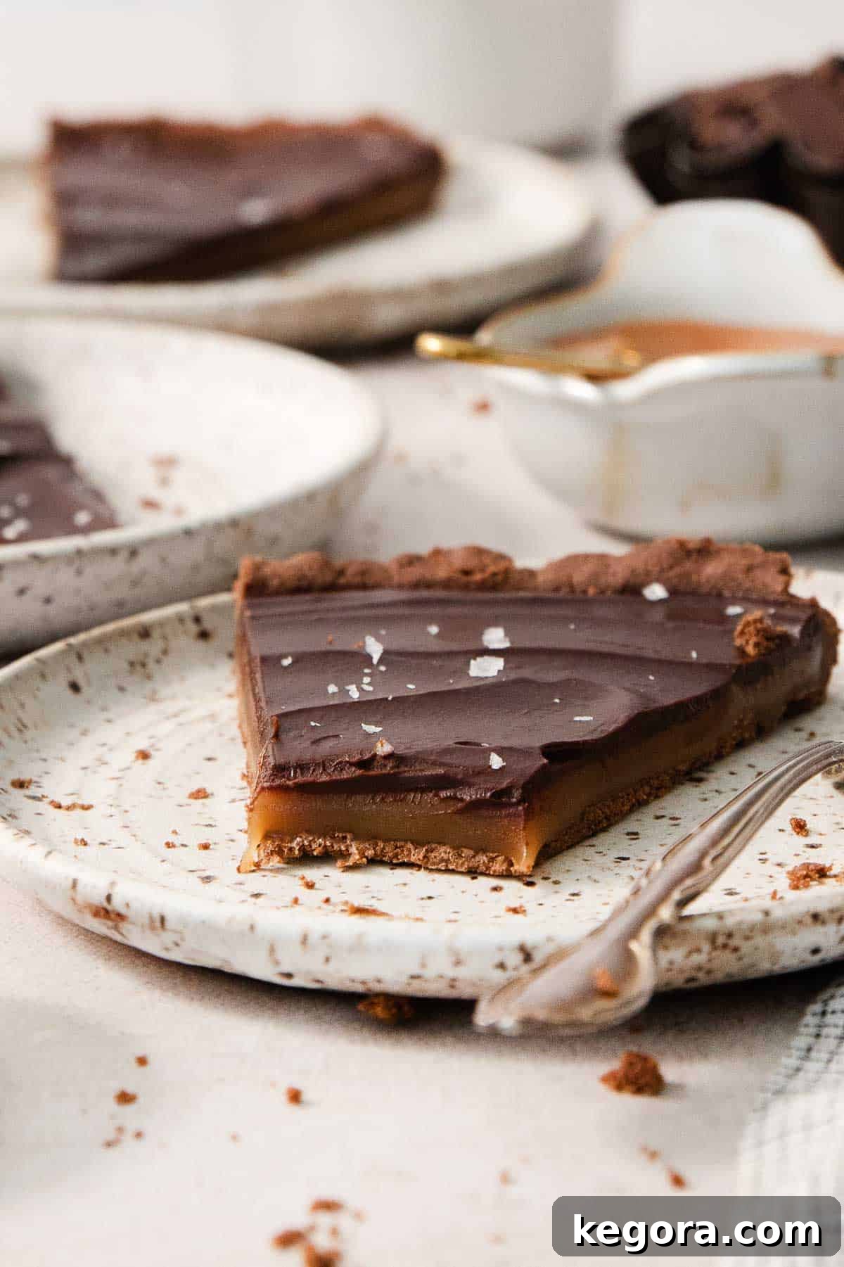 A single slice of gluten-free chocolate caramel tart served on a white plate, highlighting its rich layers