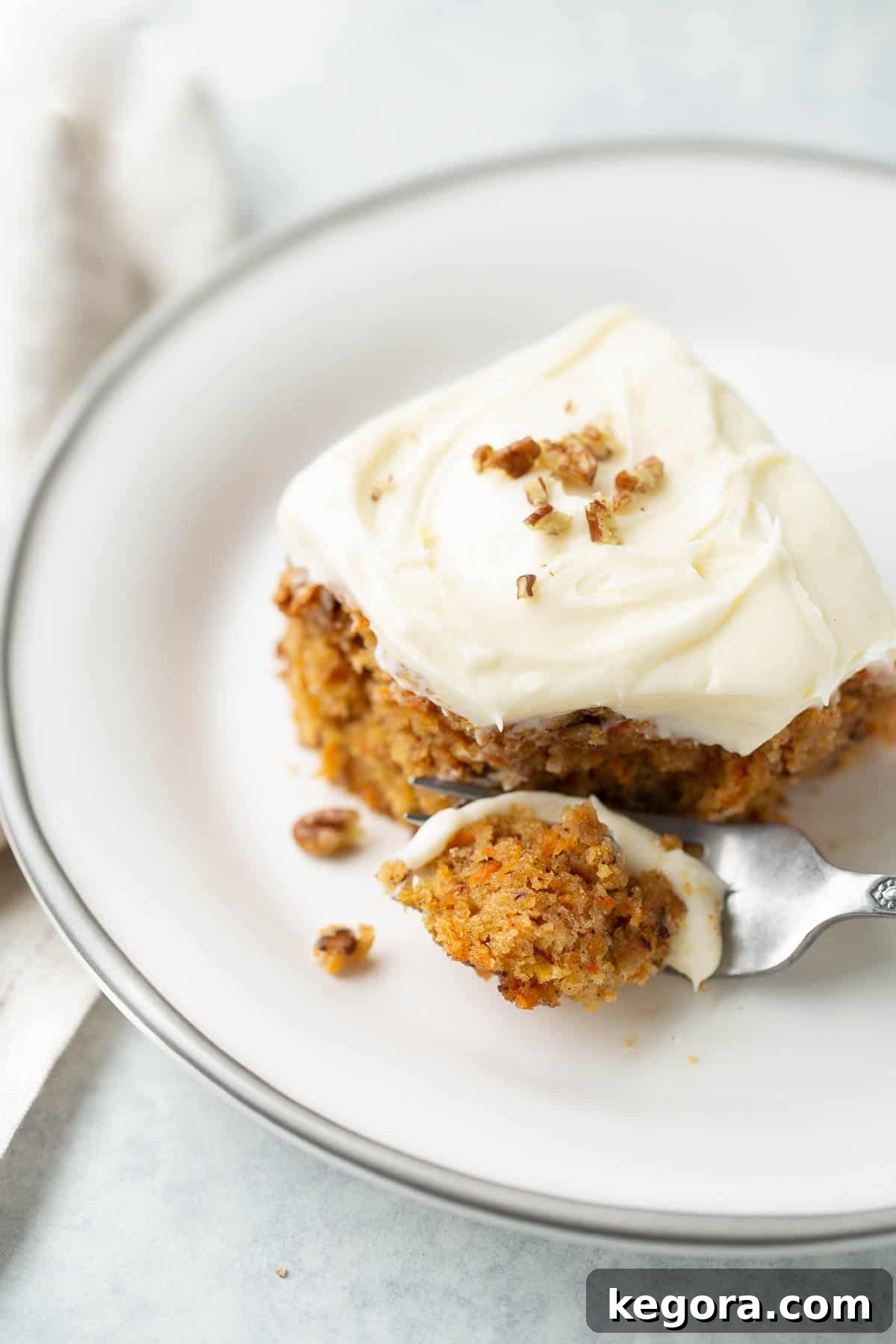 A perfectly baked slice of gluten-free carrot cake on a white plate with a fork, showing its moist texture and rich cream cheese frosting.