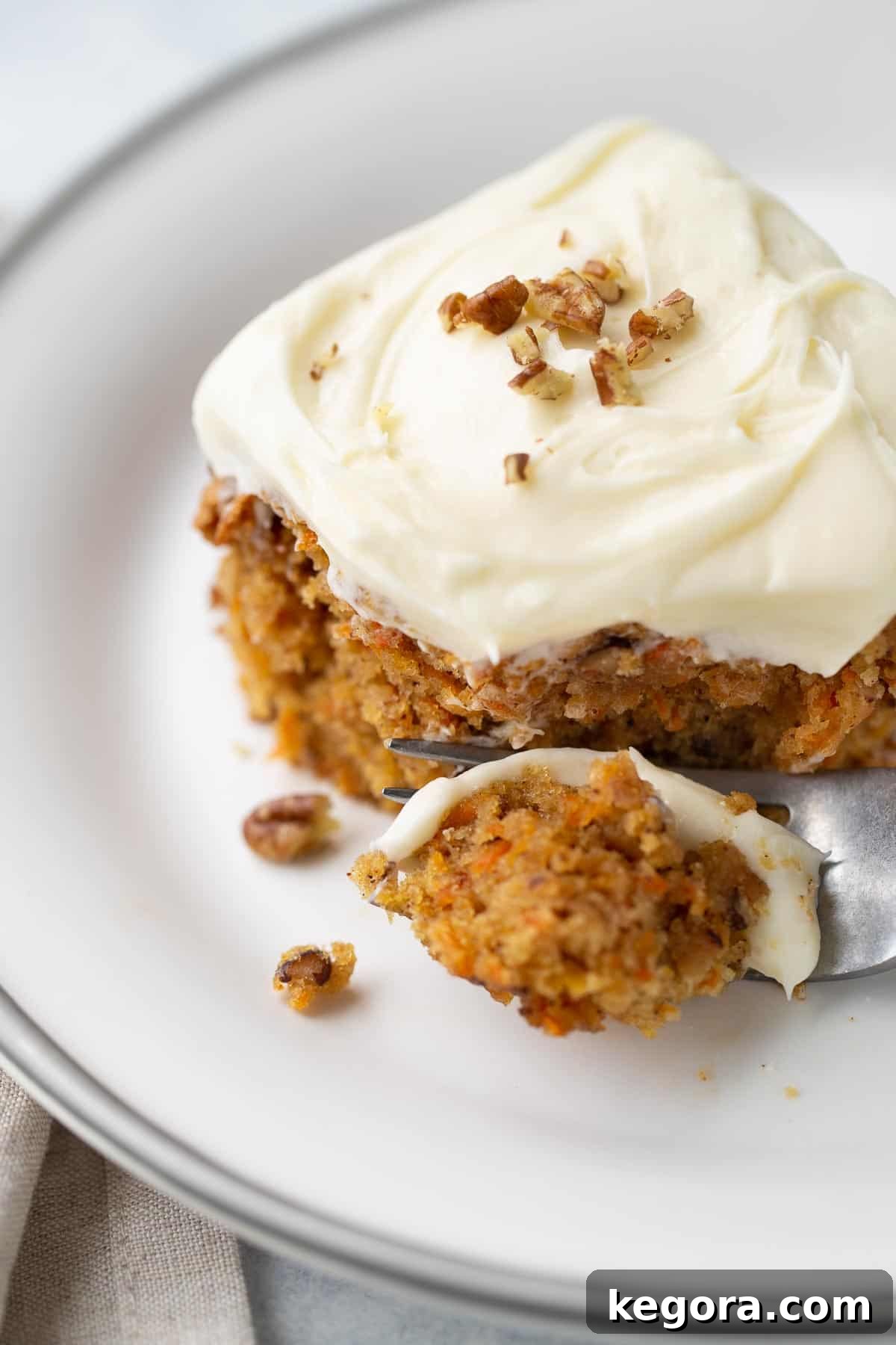 A close-up view of a thick slice of perfectly frosted gluten-free carrot cake on a white plate, highlighting the moist interior and fluffy cream cheese frosting.