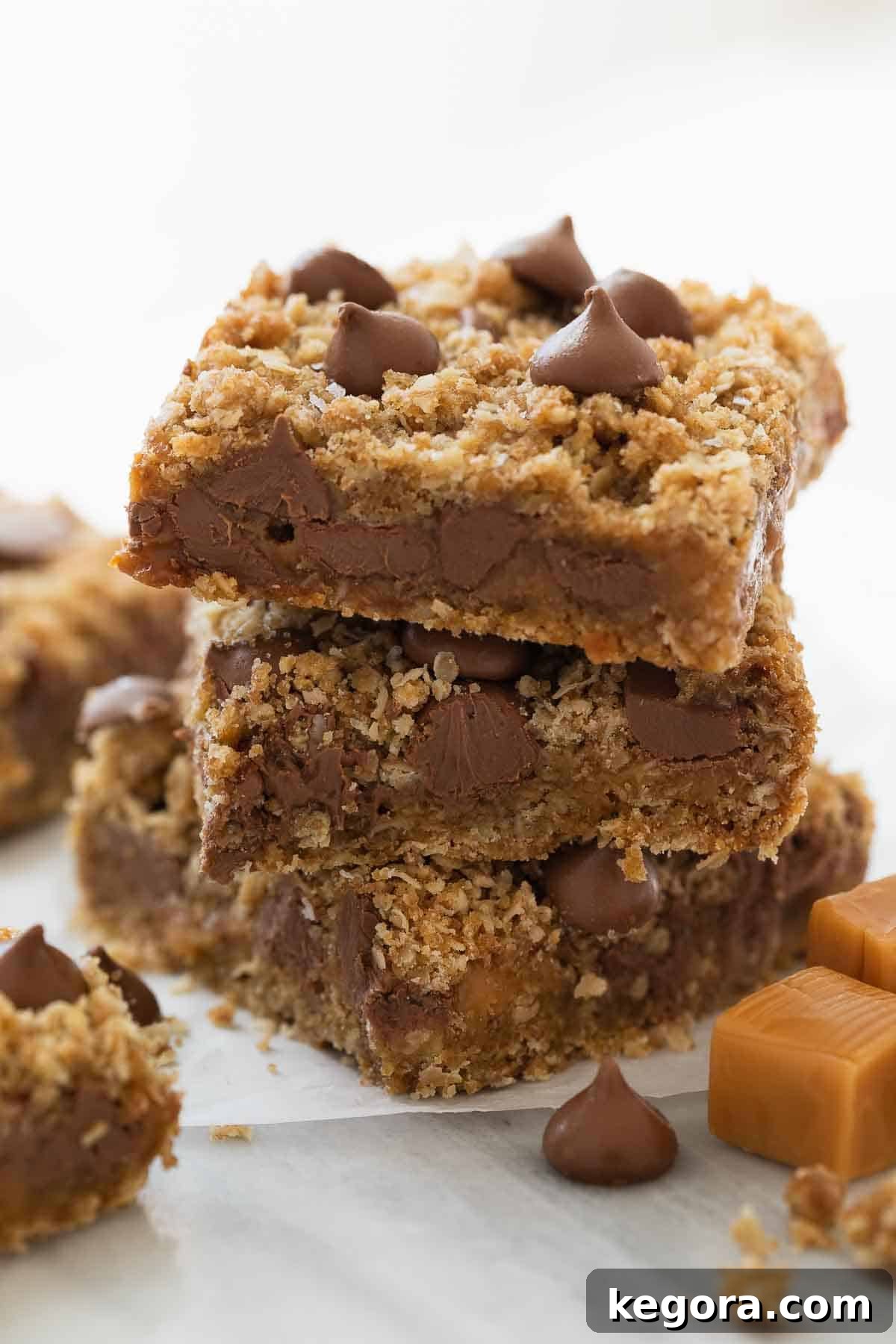 Stack of perfectly baked gluten-free oatmeal cookie bars with melted chocolate and caramel drizzle on a white marble background, ready to be enjoyed.