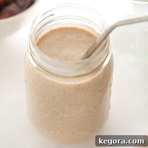 Mason jar glass filled with a delicious banana date smoothie and a metal straw, garnished for a perfect presentation.