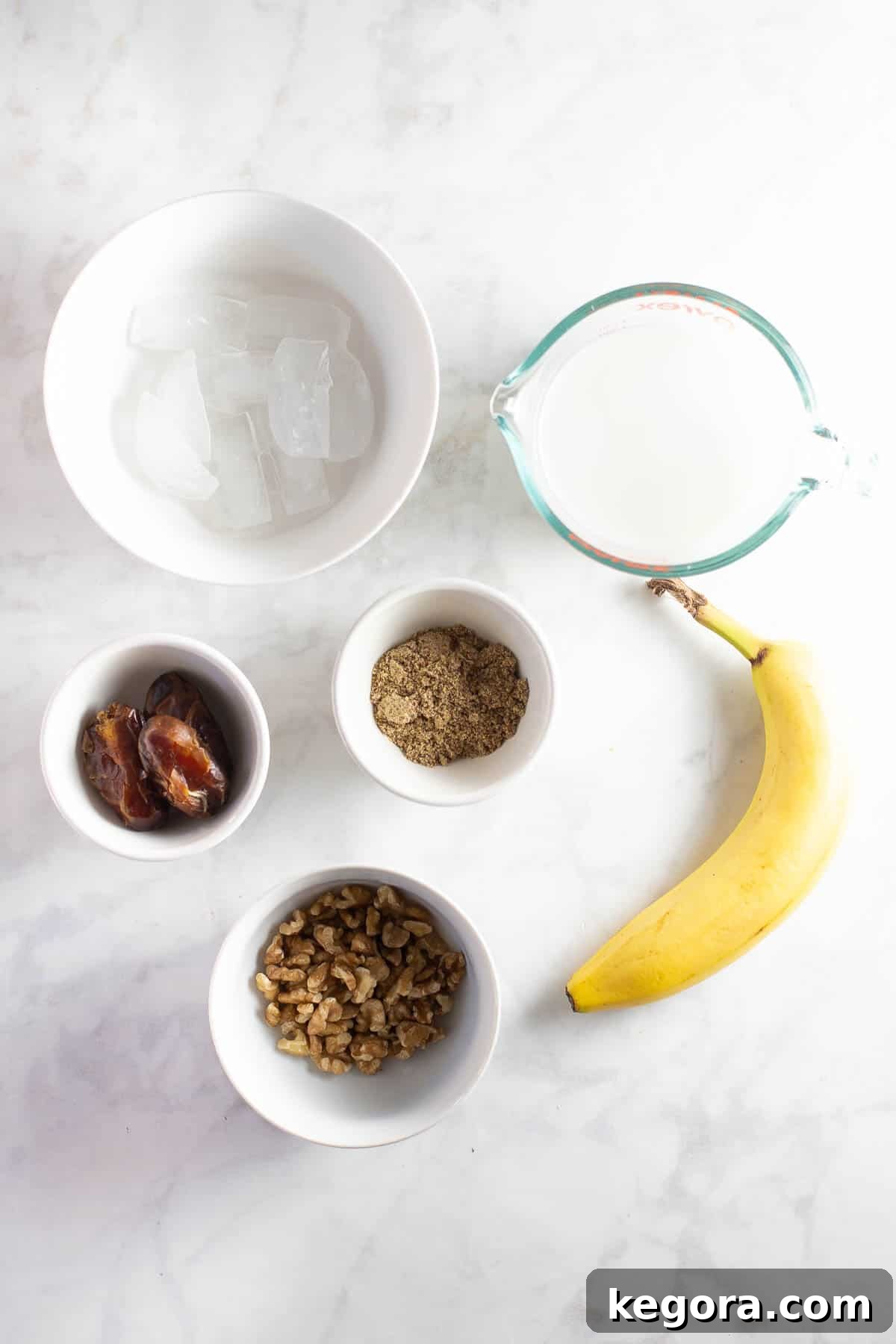 Fresh Ingredients for Banana Date Smoothie A selection of fresh ingredients, including unsweetened almond milk, frozen bananas, walnuts, flax seed meal, and dates, meticulously arranged in white prep bowls, ready to be blended into a delicious banana date smoothie.