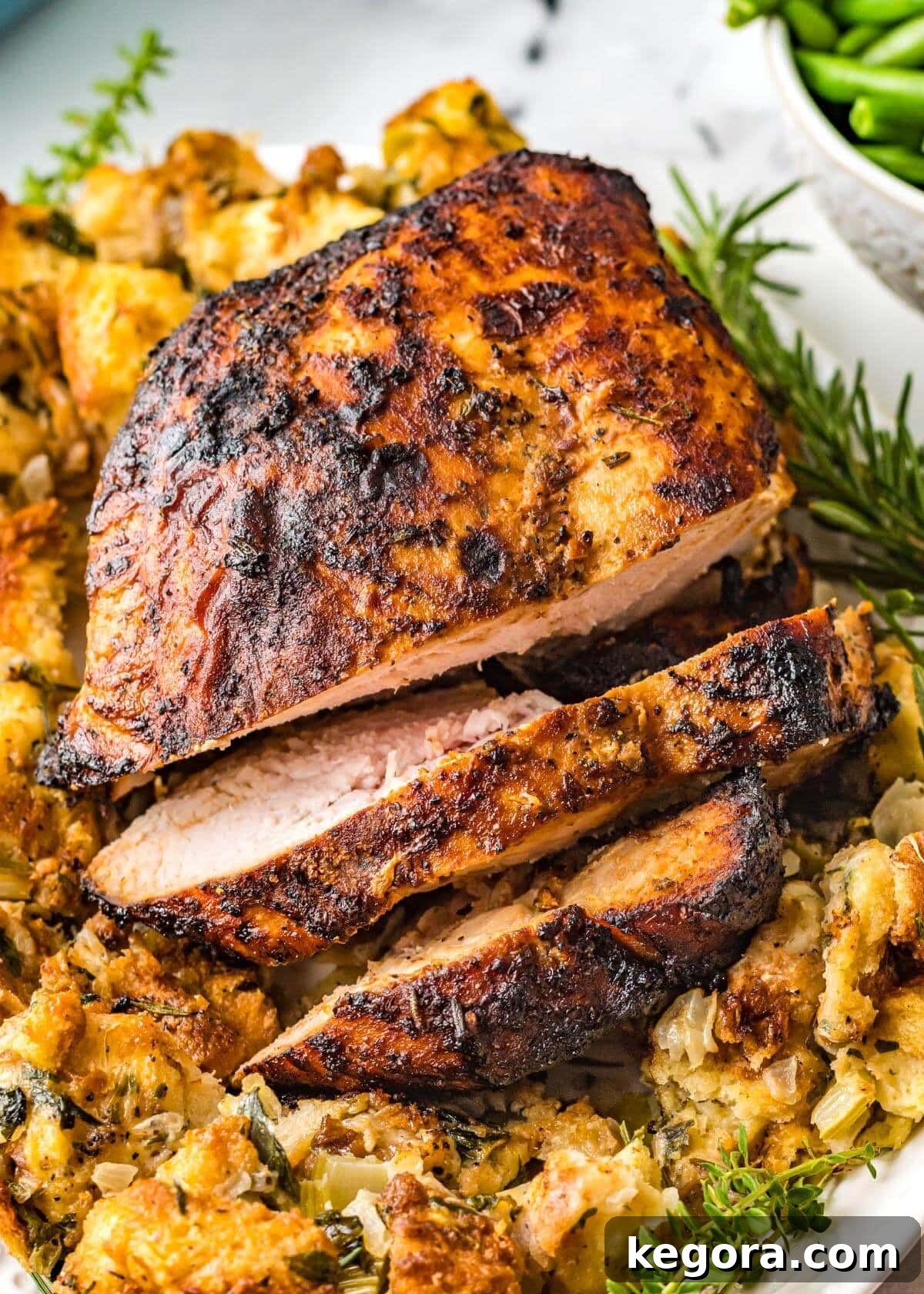 Cooked Turkey Breast on a white plate, garnished with fresh herbs, ready to be sliced.