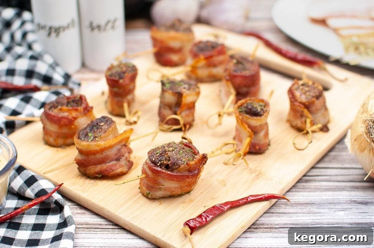 Several perfectly cooked bacon-wrapped steak bites resting on a wooden cutting board, showcasing their golden-brown crispness.