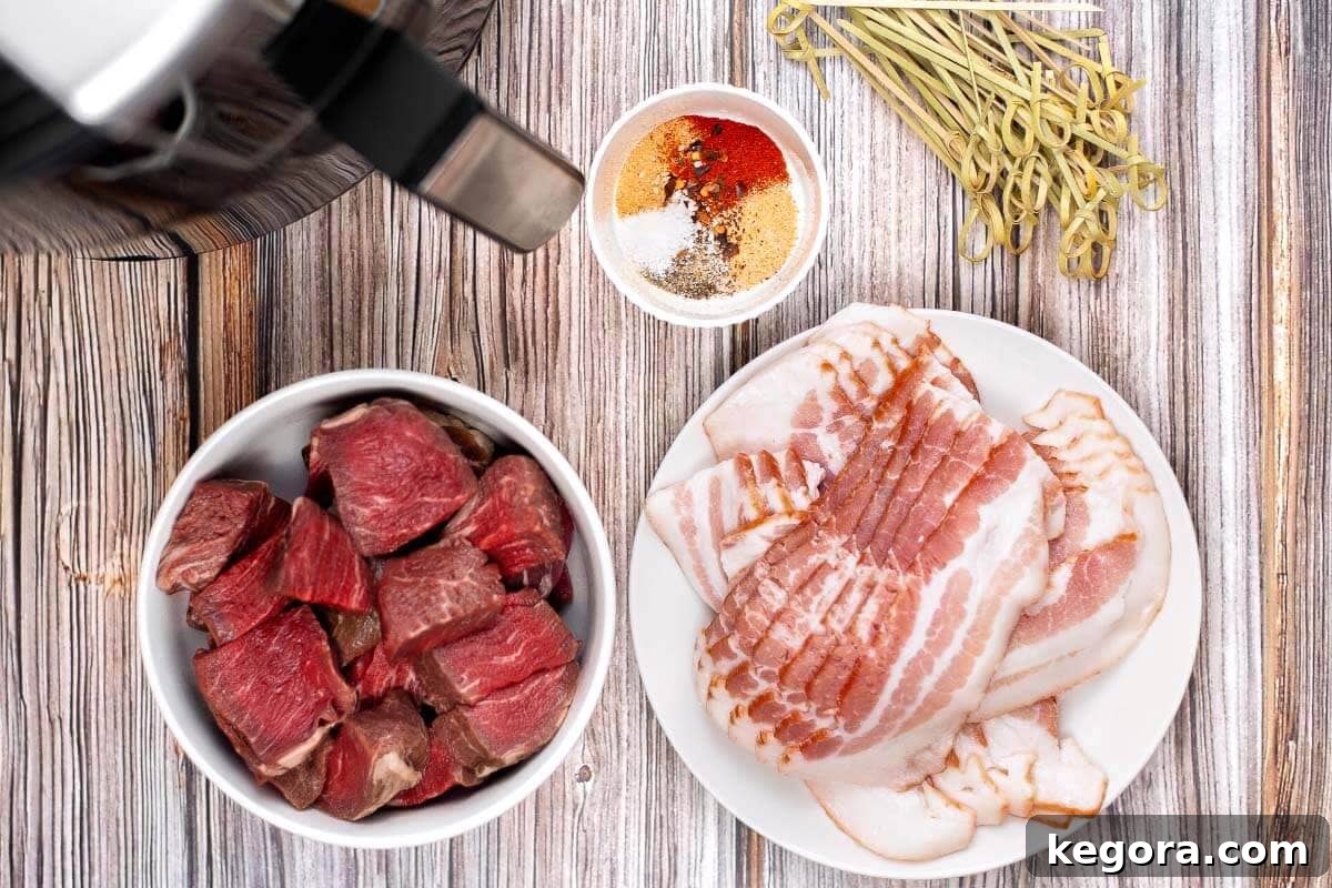 A collection of ingredients for Air Fryer Bacon Wrapped Steak Bites, including steak cubes, bacon strips, olive oil, and various spices, laid out on a wooden board.