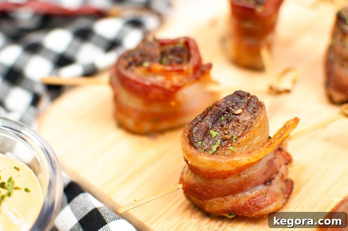 A close-up shot of a single Air Fryer Bacon Wrapped Steak Bite on a wooden board, highlighting its crispy bacon and tender texture.