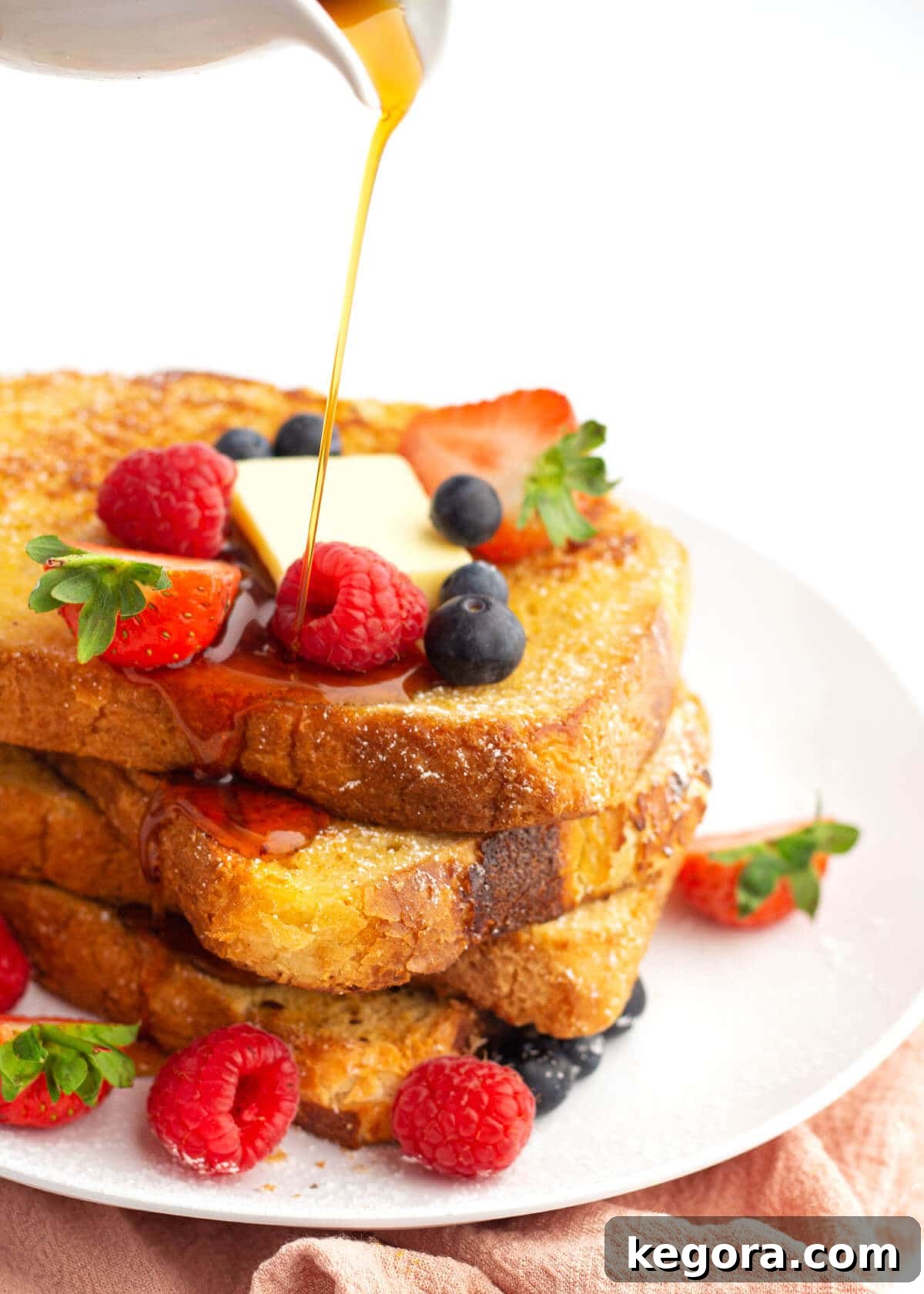 stack of french toast with berries and syrup pouring on them