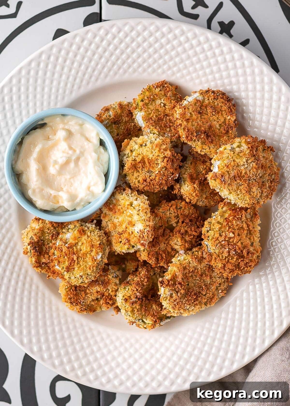 Crispy golden air fried pickles arranged artfully on a white plate, garnished with fresh herbs and a small bowl of dipping sauce beside them