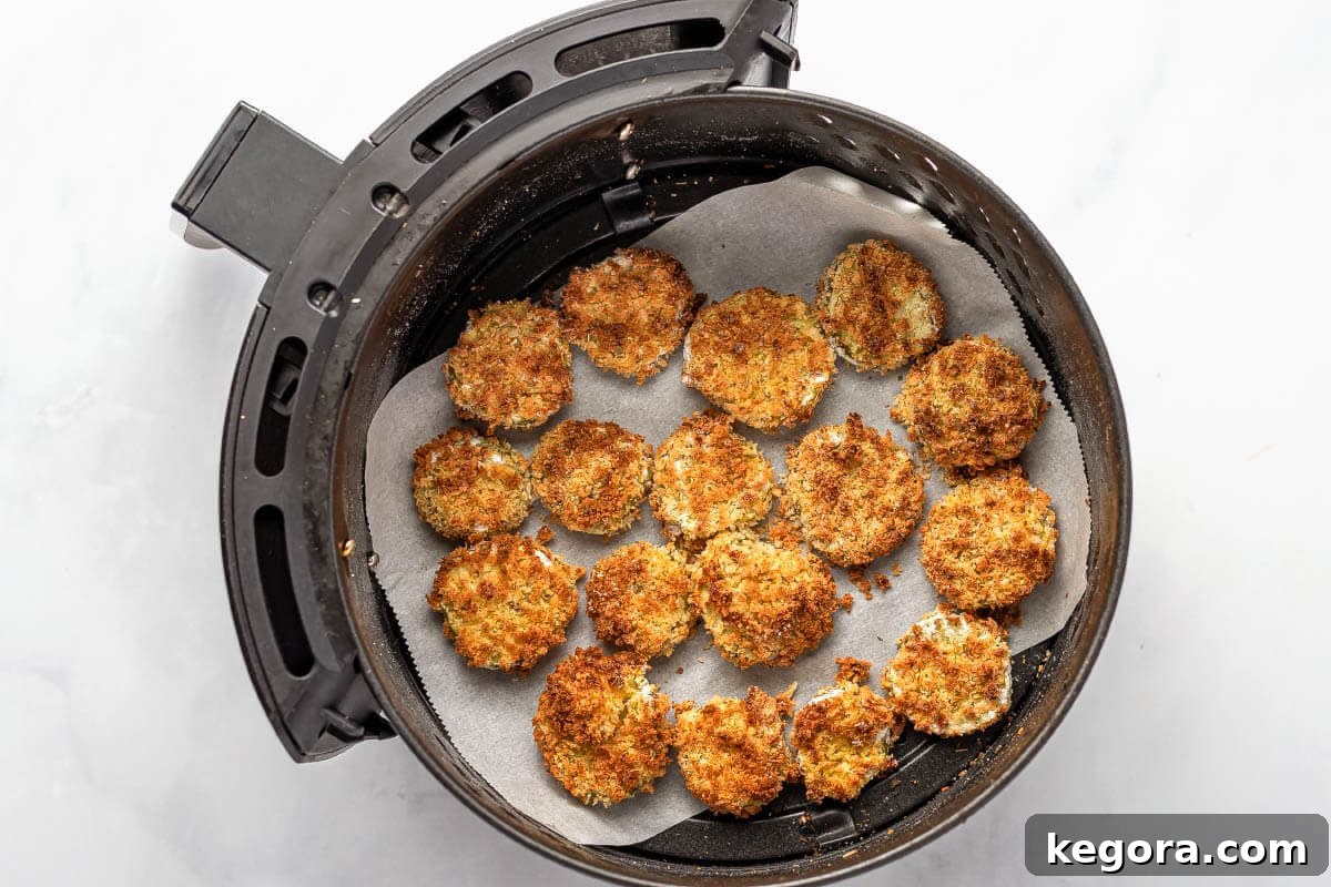 Crispy air fryer pickles cooking in a perforated parchment-lined air fryer basket, showing their golden brown texture